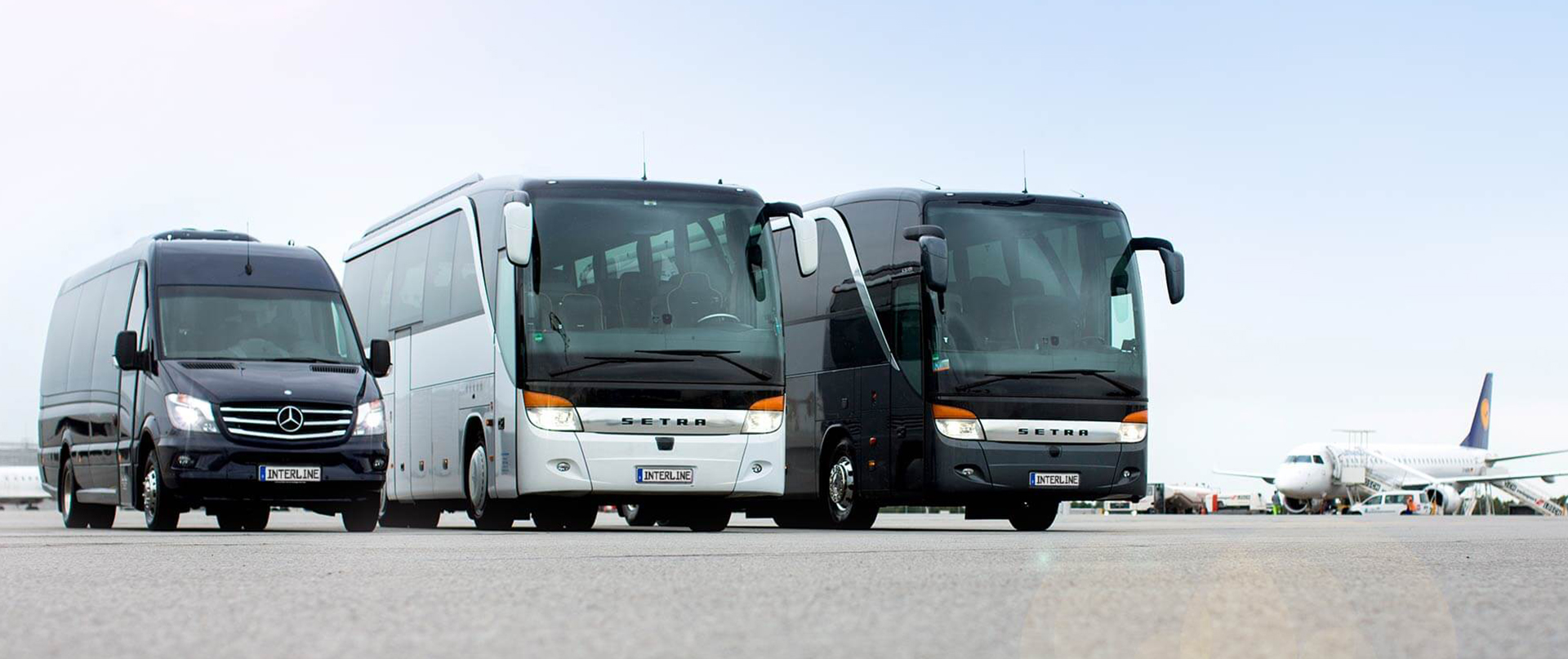 Reisebusse und Minivans auf dem Rollfeld vor einem Flugzeug.