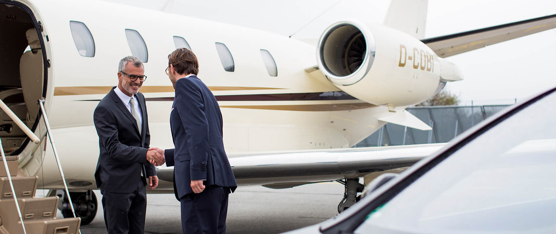 Ein Chauffeur schüttelt einem Fahrgast die Hand vor einem Business-Jet.